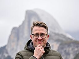 Outdoor close-up headshot of Dr Connor Robertson smiling with greenery background